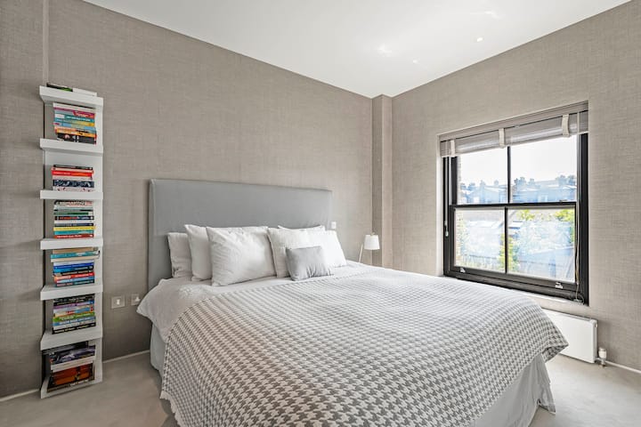 时尚明亮的卧室，配有豪华特大床、质感柔和的墙壁和一扇可以欣赏城市景观的大窗户，营造出一个平静而温馨的休憩之所，让您享受宁静的夜晚。