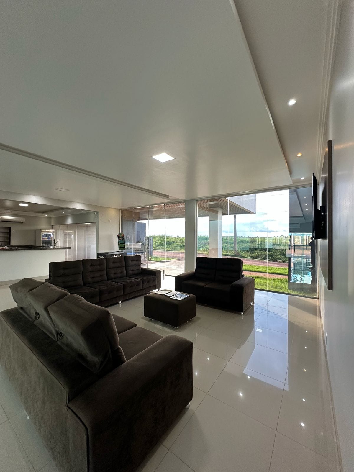 A modern living area features a layout with two dark sofas and a single comfortable chair. Large windows provide ample natural light and an expansive view of the surrounding landscape. A sleek coffee table sits in the center of the space, enhancing the contemporary design.