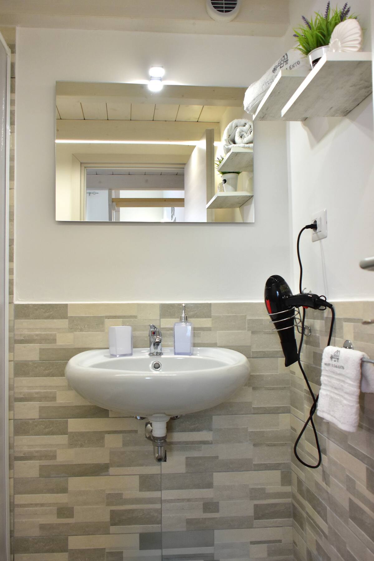 Bagno con lavabo, specchio, mensole e mosaico greige sotto il soffitto in legno bianco