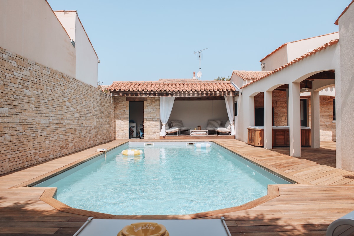 A private swimming pool is surrounded by a wooden deck, offering ample space for relaxation. Comfortable loungers are positioned nearby. The area features stylish outdoor curtains that can be drawn for added privacy. Sunlight illuminates the scene, enhancing the tranquil atmosphere.
