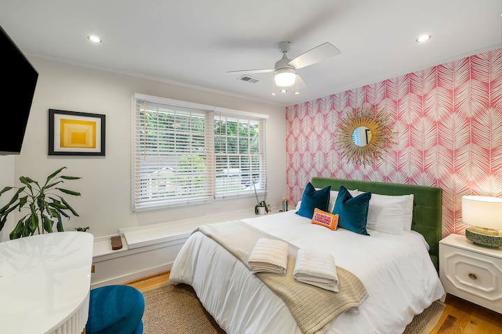 Rest easy in this vibrant bedroom with bold wallpaper, soft linens, and a peaceful view