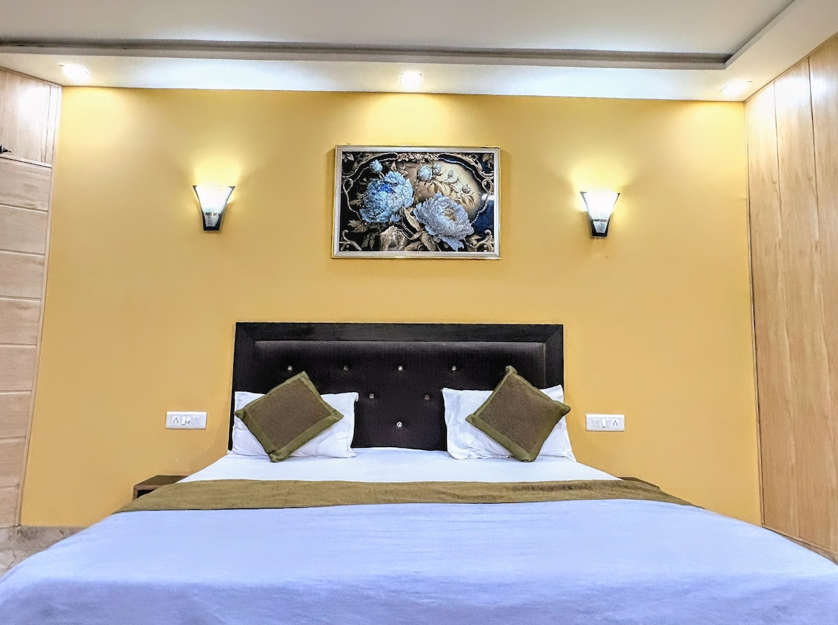 A cozy sleeping area is presented with a comfortable bed featuring two decorative pillows. Soft lighting is provided by two wall sconces, and a piece of wall art depicting shells is displayed above the headboard. The warm yellow walls enhance the inviting ambiance.