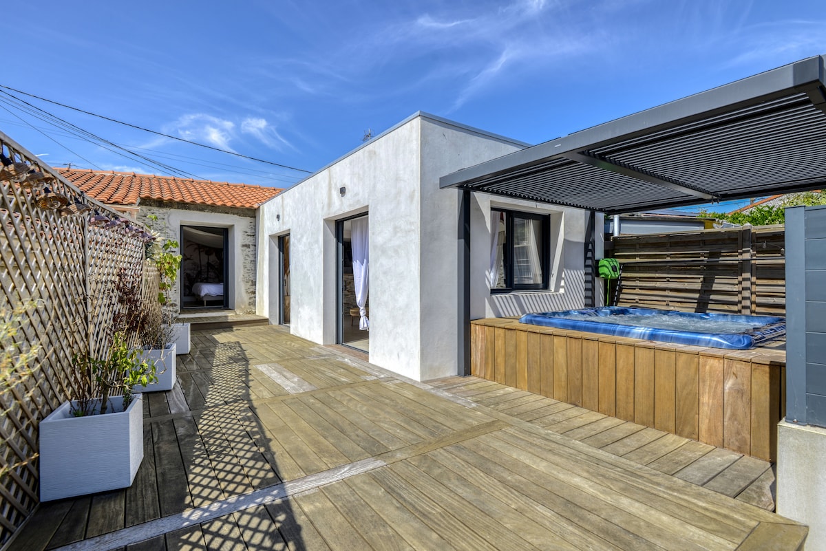 A private patio area is featured, showcasing a wooden deck and a jacuzzi surrounded by light-colored walls. Decorative planters with greenery are placed along the sides, enhancing the outdoor space. Clear skies provide ample natural light, creating a serene environment.