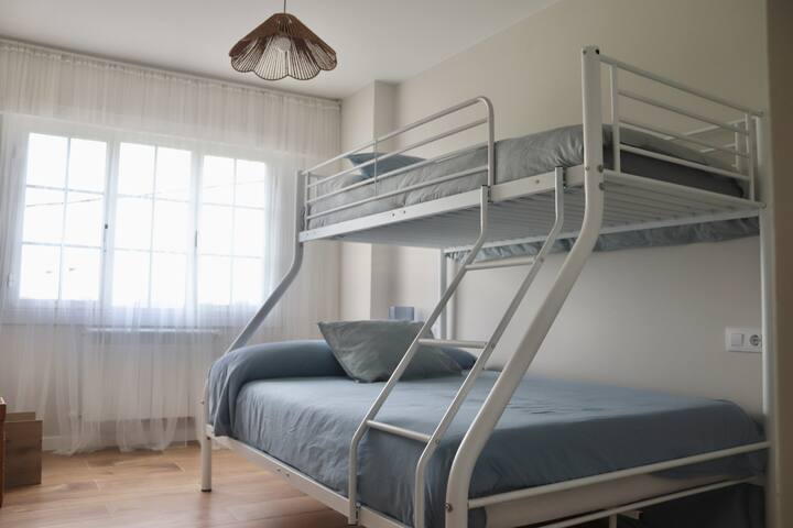 Ამ ოთახში არის ორსართულიანი საწოლი ორადგილიანი საწოლით ქვემოთ და ერთადგილიანი ზემოთ. Ფართო ჩაშენებული კარადა და საწოლთან მდგარი მაგიდა.