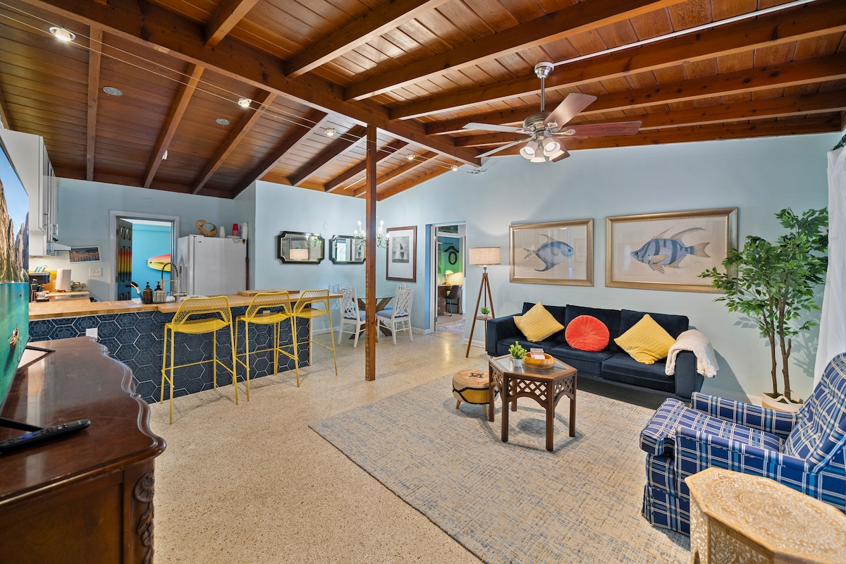 Ნათელი, პლაჟისპირა და ღია კონცეფცია! მისაღები ოთახი გამოირჩევა თაღოვანი ხის ჭერით, კომფორტული დასასვენებელი ადგილებით, ოკეანის თემაზე შექმნილი ხელოვნებითა და 50‑დუიმიანი სმარტტელევიზორით (Netflix, Amazon Prime Video და ა.შ.). Ის ჩაედინება სამზარეულოში ბარითა და მზიანი ყვითელი განავალით - იდეალურია დასასვენებლად ან ამბებისთვის.