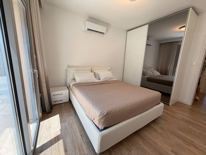 Svetlá a elegantná spálňa s luxusnou manželskou posteľou, zrkadlovým šatníkom a podlahou z mäkkého dreva.