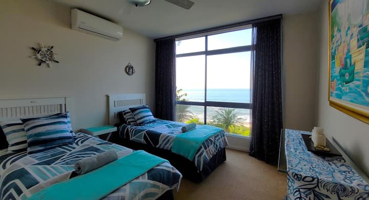 Трета спалня с две единични легла и зашеметяваща гледка към плажа и океана от прозореца.