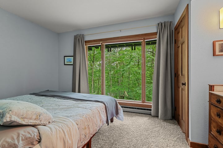 Брачна спална соба – удобно место за одмор со брачен кревет, меки сиви акценти и голем прозорец со поглед кон дрвјата. Разбудете се со сончева светлина која се филтрира низ шумата или гледајте како снегот нежно паѓа во зима.