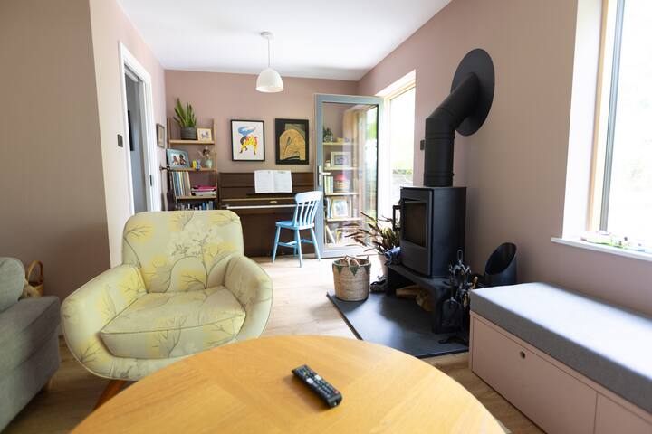 Un espacio muy relajado. Habitación relajada de color rosa oscuro con ventana con vistas al jardín tropical. Sofá, asiento de banco de ventana, piano, televisión y estufa de leña.