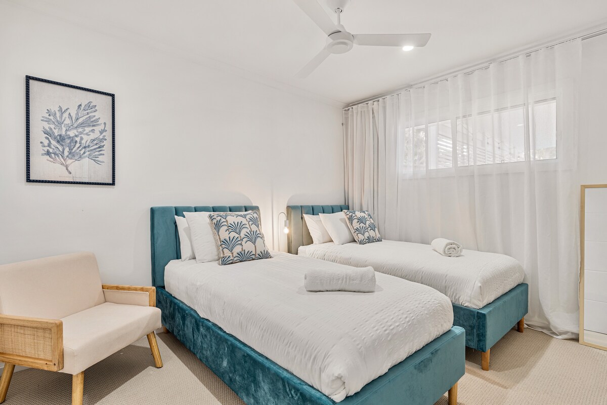 Esta habitación doble, fresca y espaciosa, cuenta con dos lujosas camas individuales con cabeceros de terciopelo, cojines de inspiración costera y suaves cortinas transparentes. Un gran espacio para que los niños o amigos se relajen con comodidad y estilo costero.