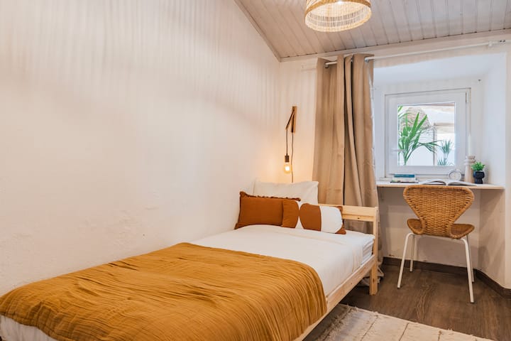 Quarto individual tranquilo com uma vibração boho e uma secretária de frente para a pérgula