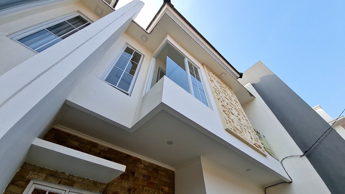 The exterior of the building is captured from below, showcasing a modern design with large windows. A decorative stone panel adds texture to the facade, while the clear blue sky creates a bright backdrop.