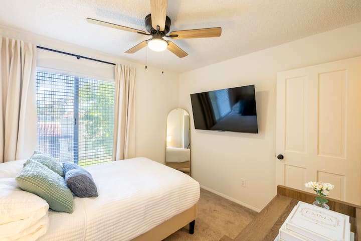 ห้องนอนที่ 1 มีเตียงขนาดใหญ่ กระจกขนาดใหญ่ ทีวีขนาด 55 นิ้ว พอร์ตชาร์จบนโต๊ะข้างเตียง นาฬิกาปลุก และม่านบังแสง