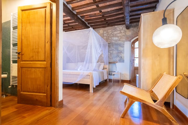 Cama tamaño king con mosquitera y marco, baño privado con ducha, armario, silla, mesitas de noche, lámpara, espejo de cuerpo entero, puerta privada a la terraza exterior.