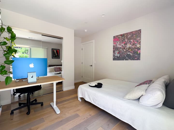 Acogedor dormitorio con una oficina en casa funcional, luz natural brillante, suelos de madera, decoración minimalista, una estantería completa y patio privado, ideal para trabajar desde casa y estancias cómodas.

