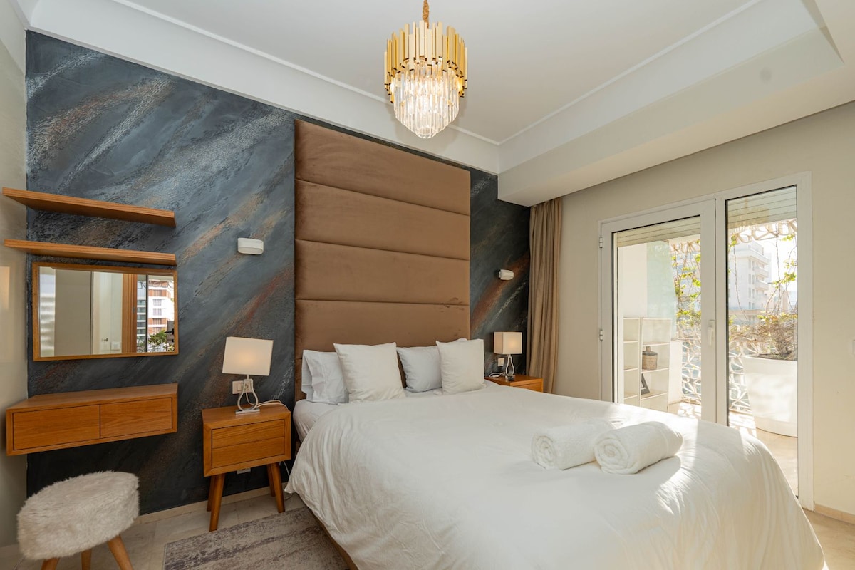 Lichte kamer met kingsize bed, gestoffeerd hoofdeinde, moderne wanddecoratie en directe toegang tot het balkon met uitzicht op de stad.