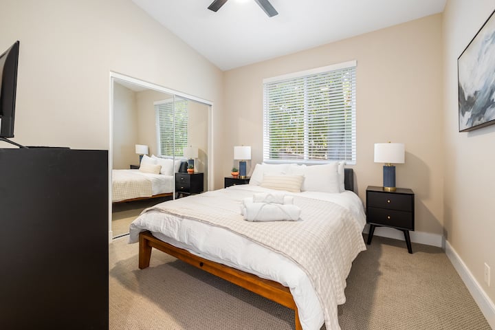 ห้องนี้มีเตียงนอนที่สะดวกสบายพร้อมผ้านวมและหมอนสีอ่อน ขนาบข้างด้วยโต๊ะข้างเตียงสองข้างที่เข้ากัน โต๊ะข้างเตียงแต่ละตัวมีโคมไฟที่มีฐานสีเข้มและที่บังแสงสีอ่อนอย่างมีสไตล์