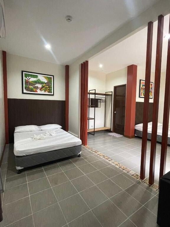 A spacious family suite is presented, featuring a large bed with crisp white bedding and an additional sleeping area separated by wooden slats. Wall art adorns the walls, and a closet is visible in the corner, adding functional space for belongings.