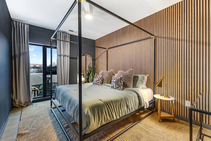 Modern and serene bedroom with a sleek canopy bed, warm wood accents, and private balcony access—your cozy urban escape.