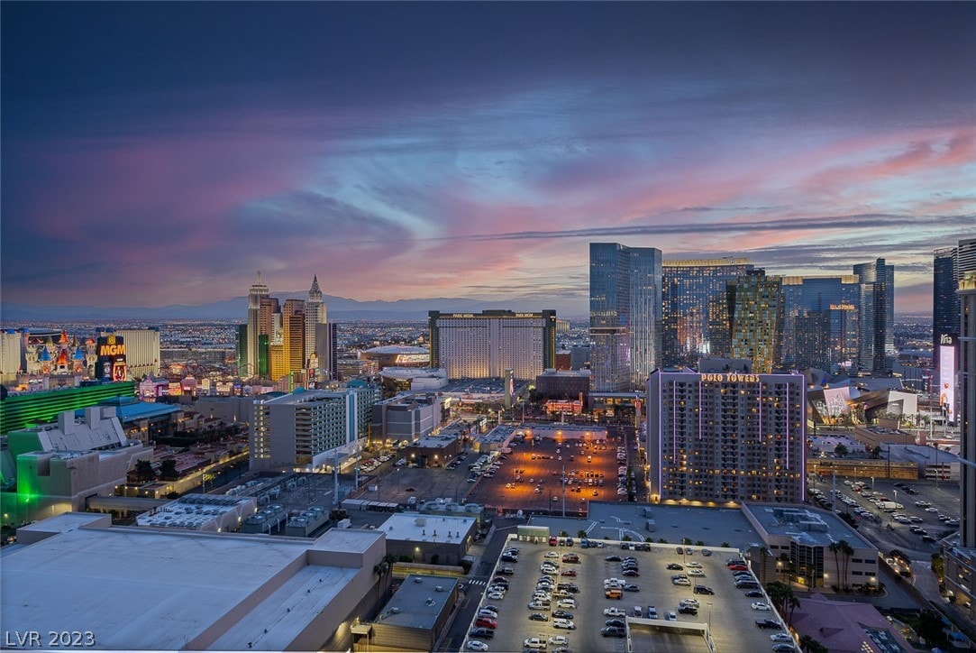 A panoramic view of the Las Vegas skyline at sunset, showcasing a vibrant array of colors in the sky. Notable buildings and attractions of the Strip are visible, along with the surrounding mountains in the distance, providing an expansive urban landscape.