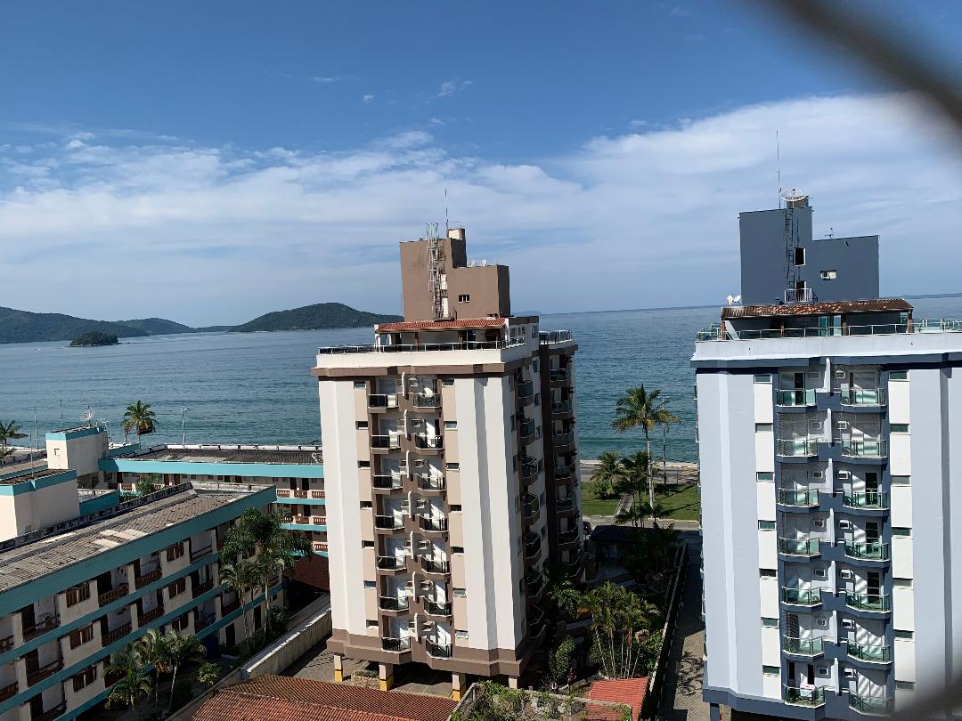 The image captures a serene coastal view from a high vantage point, showcasing two residential buildings and the ocean in the background. Clear blue skies are visible above, with a distant island and palm trees enhancing the tranquil seaside atmosphere.