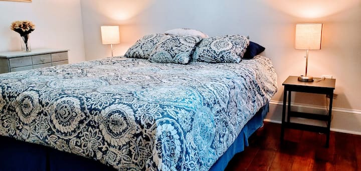 The bedroom has a queen bed, ceiling fan, two (2) bed-side tables with lamps, a small dresser, a full size closet with hangers, a luggage rack, and blackout window curtains.