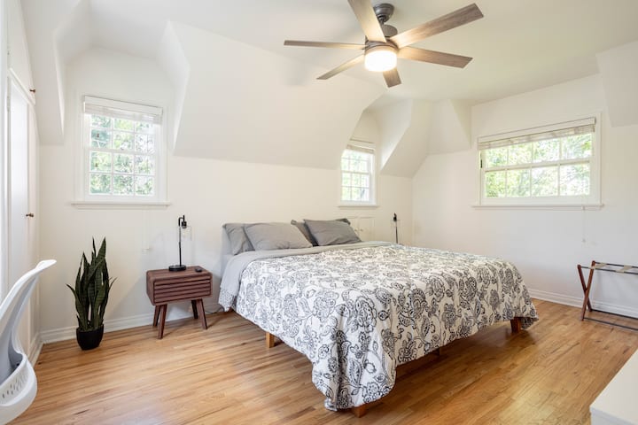 	-	Habitación luminosa con ventanas
	• 	Cama tamaño Cal King
	• 	Esquema de color gris y blanco
	• 	Mesas de noche de madera en los lados de la cama
	•	Ventilador de techo con luz
	-	Suelos de madera.
	-	Planta en maceta
	•	Escritorio y silla
	•	Diseño minimalista y espacioso