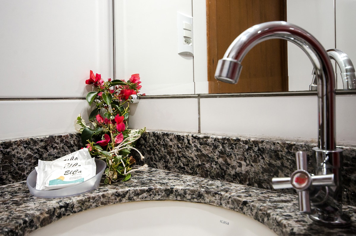 A granite bathroom countertop is equipped with a modern faucet and a small decorative arrangement of pink and green flowers. A neatly placed soap dish displays toiletries, complemented by the sleek design of the mirror above.