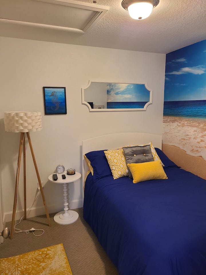 Средна спалня с двойно легло и стенопис на плажа на една стена.