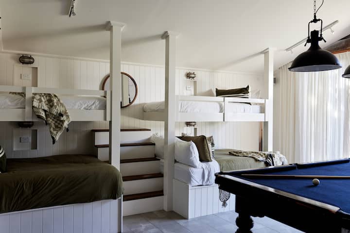 The Bunk House.  Custom made Bunk beds with 2 double and 2 single beds with comfy linen.  Each bed with own usb ports and bedsides. Air conditioning, 75" Samsung Smart TV, Sonos, Pool Table, Ping Pong & Surfboard storage.  