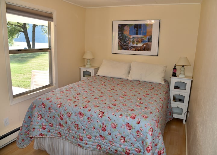 Dormitorio con cama tamaño queen, armario pequeño y vistas al río desde la ventana.