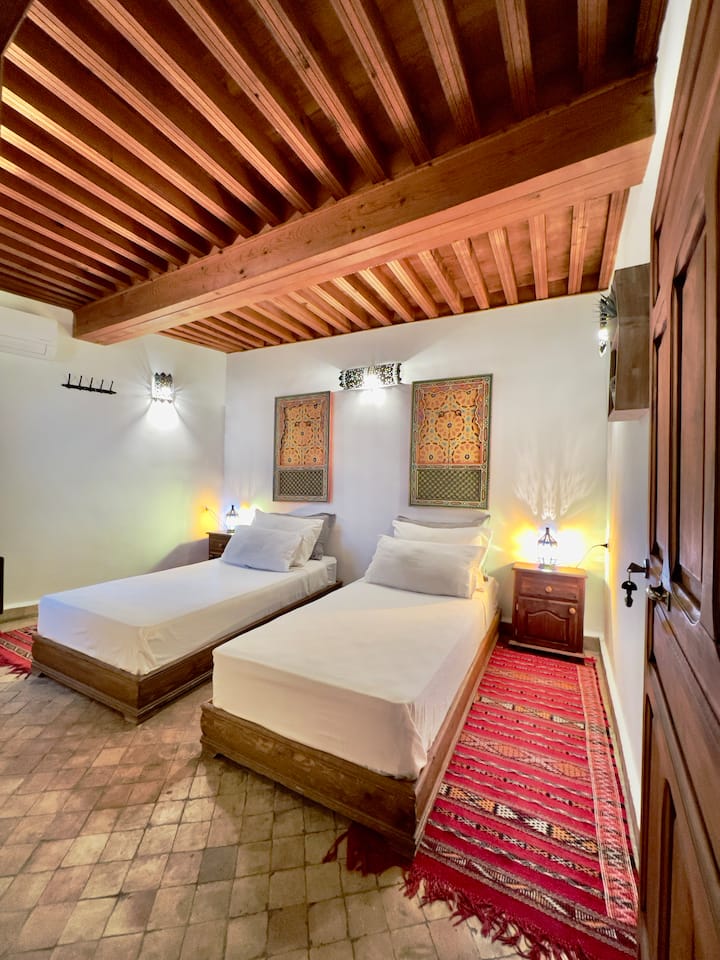 Chambre principale avec literie haut de gamme pour des nuits reposantes, deux lits simples réglables, une salle de bain extérieure, une fenêtre avec vue sur le patio.