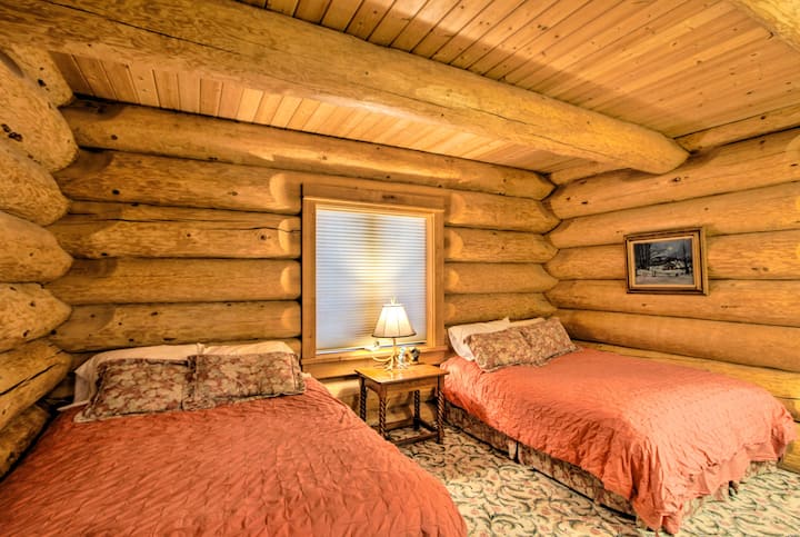 The downstairs bedroom offers two spacious queen beds with peaceful forest views from both windows. A generous closet and open layout add comfort, while hand-carved log walls and a handcrafted antler lamp bring warmth, charm, and rustic luxury.