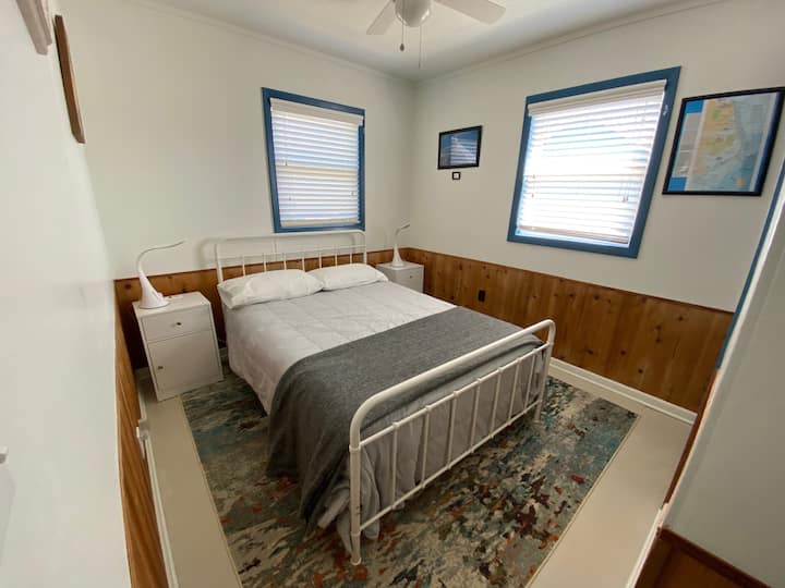 เตียงใหญ่ตู้เสื้อผ้าพร้อมชั้นวางของชั้นวางสัมภาระและพัดลมเพดาน  โคมไฟข้างเตียงมีแสงสว่างที่ปรับได้พร้อมพอร์ตชาร์จ USB 2 พอร์ต พอร์ตชาร์จและปลั๊กไฟเพิ่มเติมอยู่บนโต๊ะข้างเตียงและพอร์ต USB บนเต้าเสียบผนังไฟฟ้า