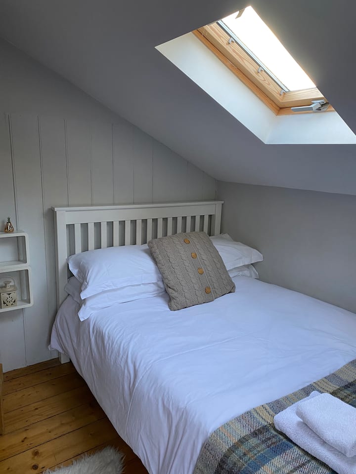 غرفة النوم الصغيرة المريحة في الجزء الخلفي من الكوخ التي تطل على المنطقة المشجرة في الجزء الخلفي من الكوخ.