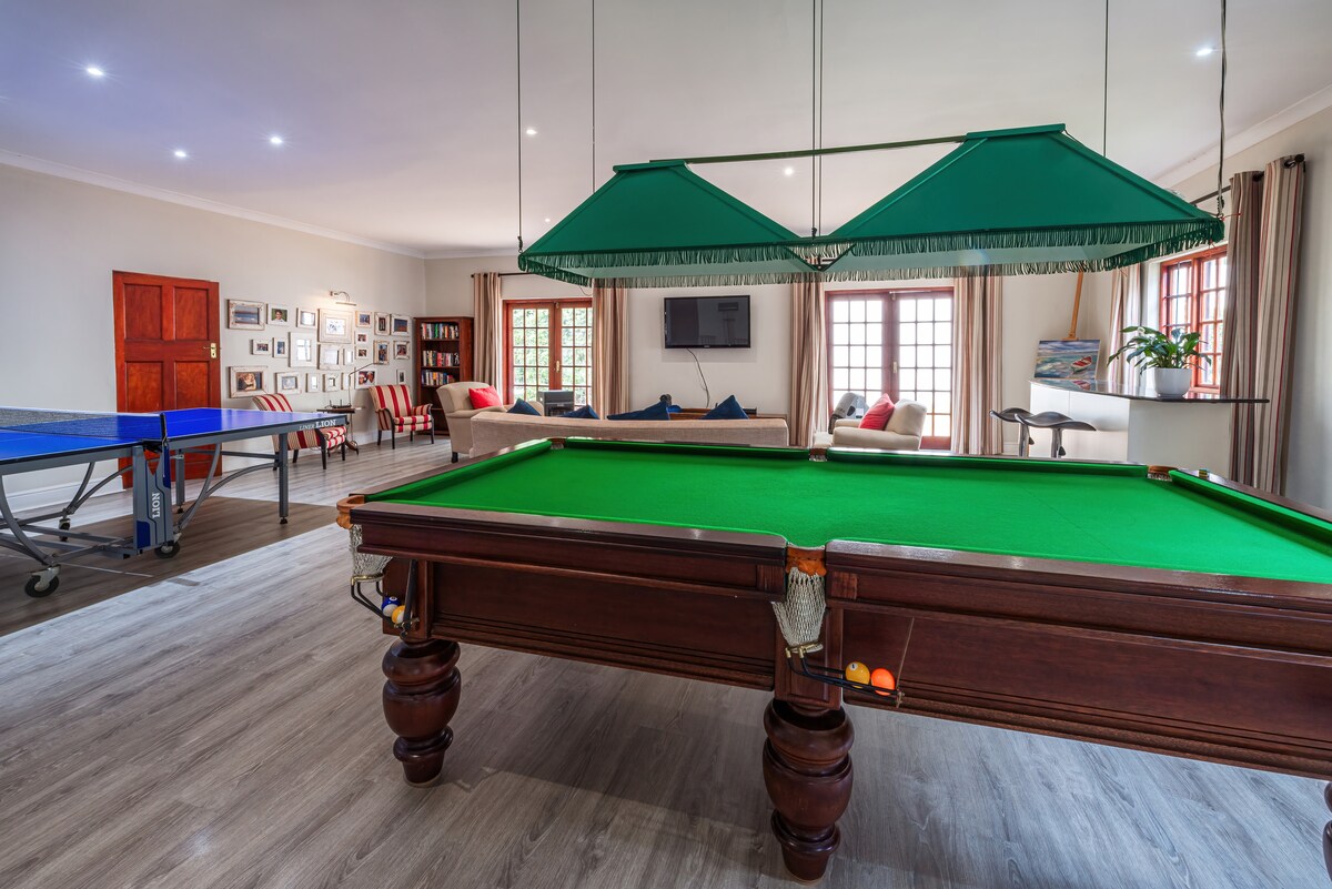 A spacious living area features a billiard table and a table tennis table positioned beside large windows that allow natural light to fill the room. Comfortable seating is arranged nearby, creating a relaxed environment suitable for leisure activities.