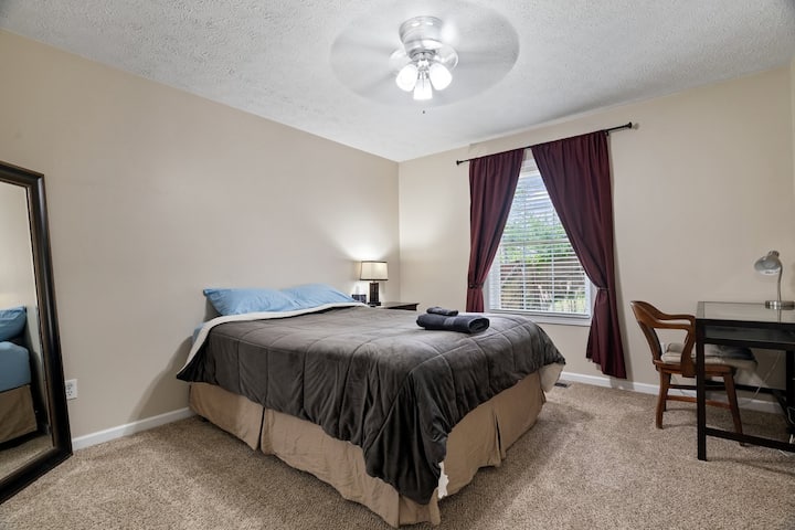 Chambre d'hôtes n °1 avec lit Queen Size, télévision murale, ventilateur au plafond, miroir de dressing, table de nuit, lampe, prise USB, bureau avec chaise et lampe, rideaux occultants, sol recouvert de moquette, placard avec cintres et porte de verrouillage.