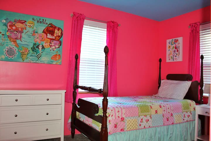 The Pink Room- Twin Bed. Located in the downstairs hallway with small dresser, nightstand, and lamp.