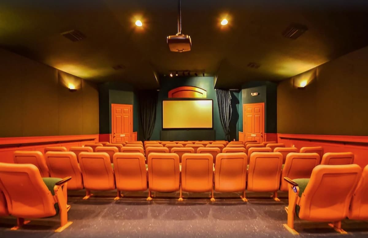 A private movie theater is equipped with tiered seating arranged in rows. The walls are adorned in dark colors, contributing to a cozy atmosphere. A large screen is positioned at the front, complemented by dim lighting and soundproof features for an immersive viewing experience.