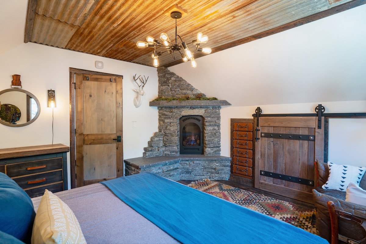 Primary Bedroom-Romantic setting with private gas fireplace.  Live Edge handcrafted headboard with rock and resin. Built-in leather dresser. Modern/Industrial dresser. Leather Loveseat. Handcrafted barn track door to closet. Bedroom on top floor