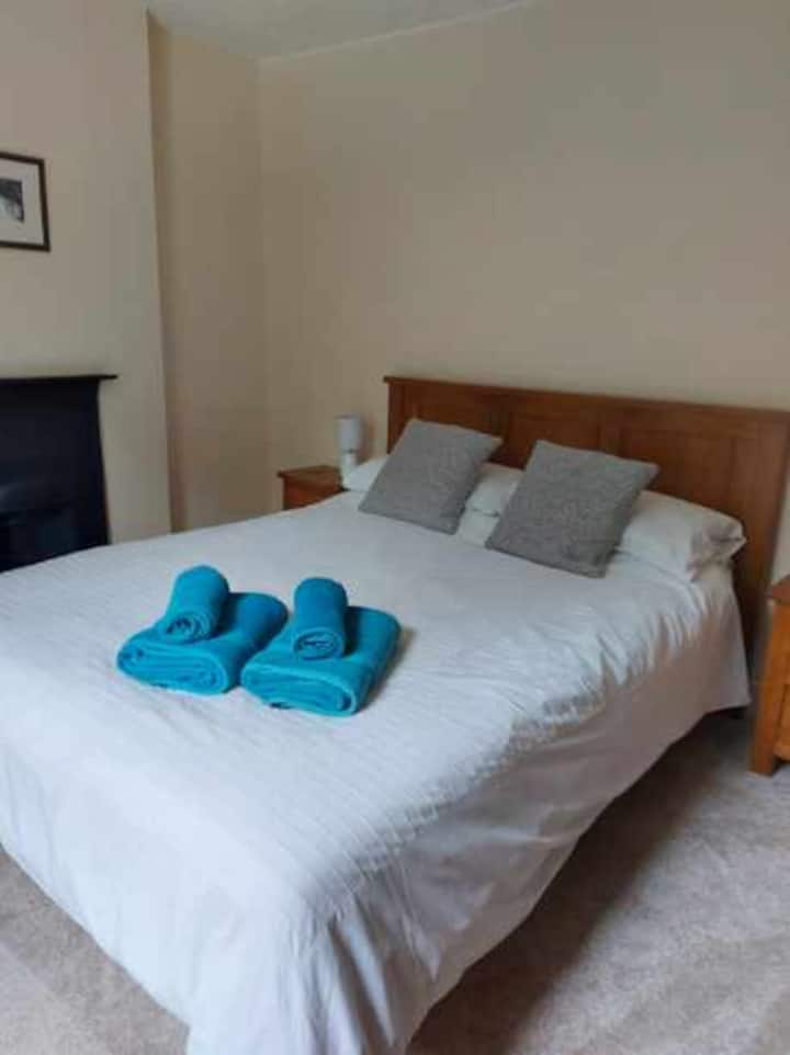 ห้องนอนใหญ่พร้อมเตียงขนาดคิงไซส์ตู้ลิ้นชักและตู้เสื้อผ้าโบราณและโต๊ะข้างเตียงไม้โอ๊คและตู้เสื้อผ้า  ห้องนี้มีหน้าต่างด้านหน้าของบ้านและมองออกไปยังพื้นที่เพาะปลูก

