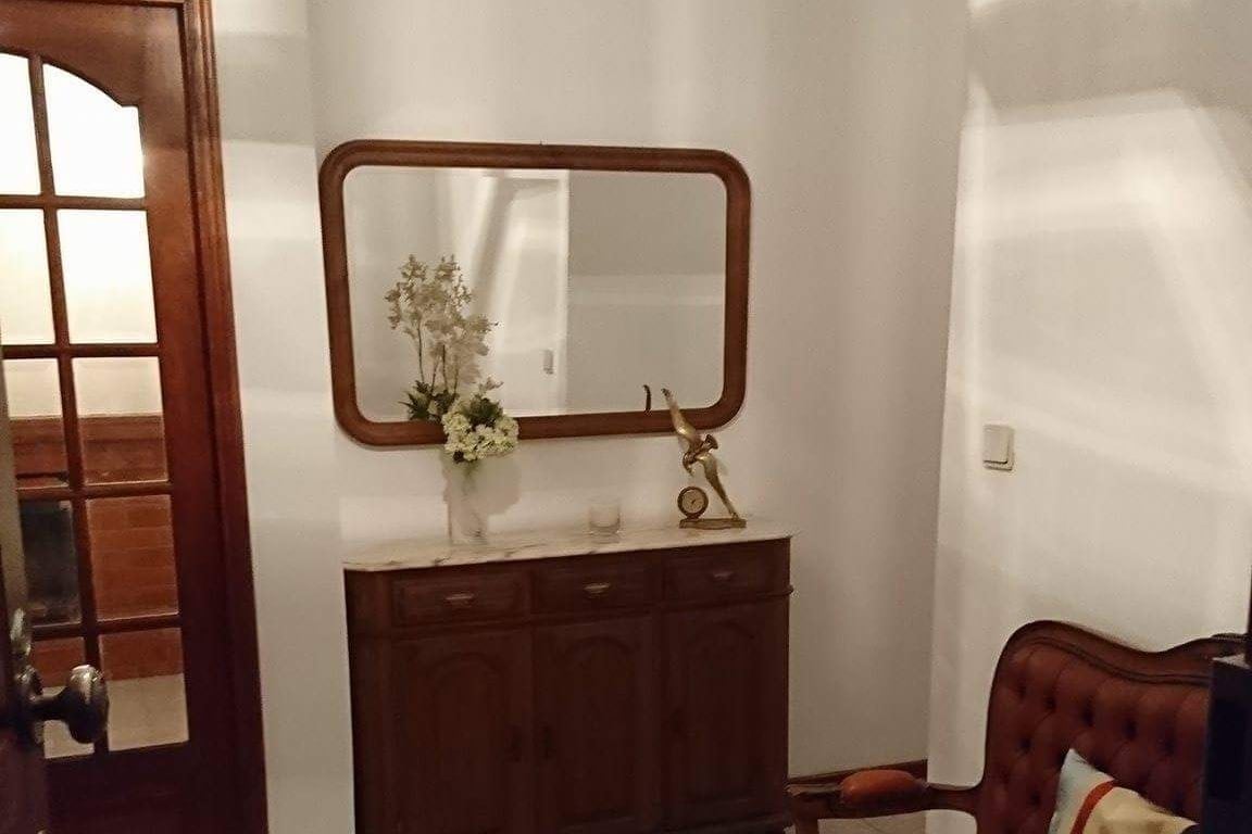 A welcoming entryway features a wooden console table adorned with a vase of flowers. Above the table, a large mirror reflects the soft lighting. The space is complemented by a classic upholstered chair, providing an inviting atmosphere for guests.