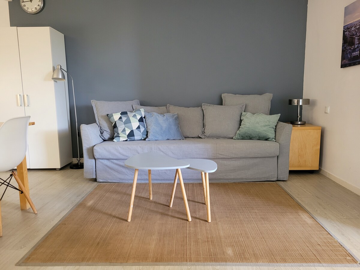 A comfortable living area is showcased, featuring a spacious sofa adorned with various decorative pillows. A small coffee table is positioned in front, resting on a textured area rug. A lamp and a modern side table add functional elements to the neutral-toned space.