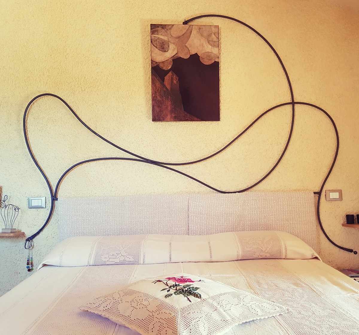 A spacious bed is positioned against a textured wall, featuring an artistic display of abstract shapes above. Decorative elements include a pillow with floral embroidery and flowing lines that create a unique visual interest, complementing the inviting atmosphere of the room.