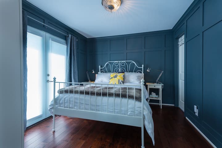 Dormitorio número 1 con armario, luz nocturna, persianas y cortinas, 2 mesitas de noche con lámparas y una cómoda cama tamaño queen.