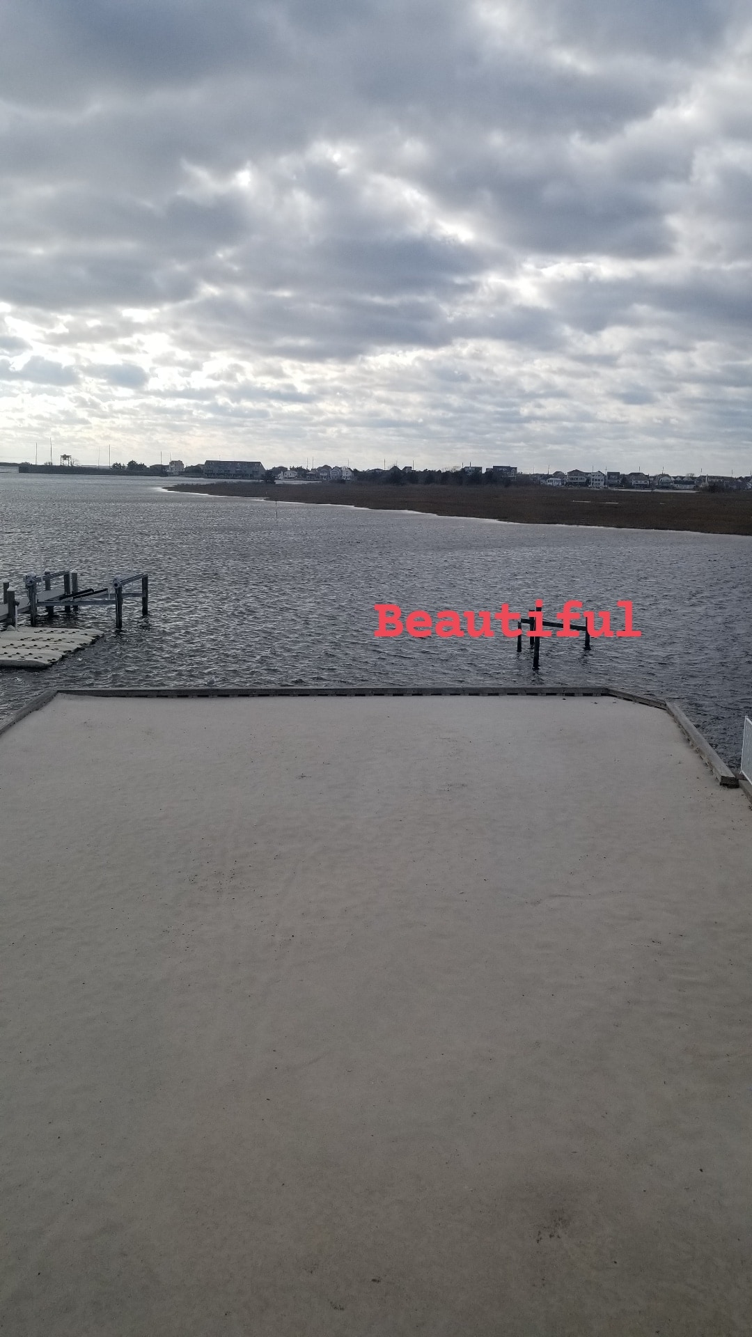 A view of the water is showcased, with gentle waves reflecting soft light under a cloudy sky. A wooden dock extends into the water, providing a serene backdrop. The surrounding area includes distant land, offering a tranquil atmosphere.