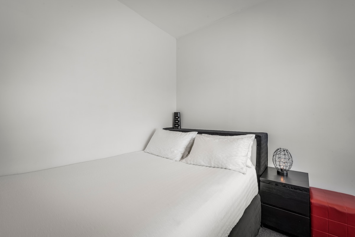 מיטת קווין סייז, שולחנות ליד המיטה, מנורה ליד המיטה, קולבי בגדים וארון בגדים.