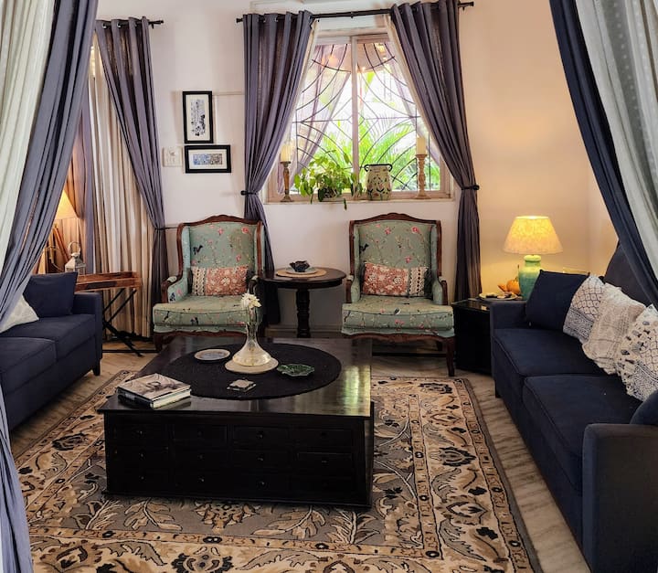 Living Room with Hardwood Comfortable Couches, High Chairs, and Plush Carpet. This Room gets Ample Natural Lighting through the Old Portuguese style Windows