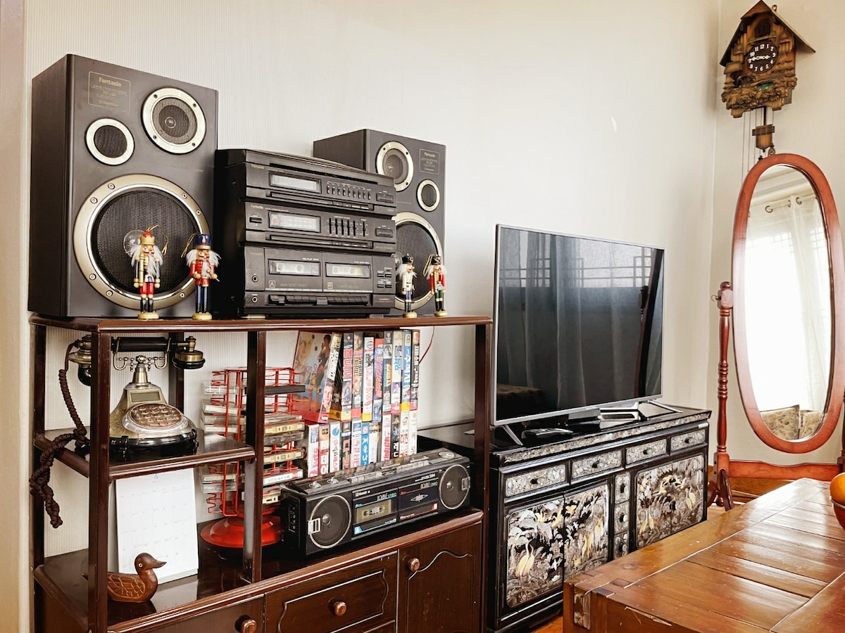 A vintage entertainment unit showcases a stereo system, speakers, and a television. Nearby, a mirrored cabinet adds depth to the room. Decorative elements include two nutcracker figures and an old-fashioned telephone, creating a space rich in character and nostalgia.