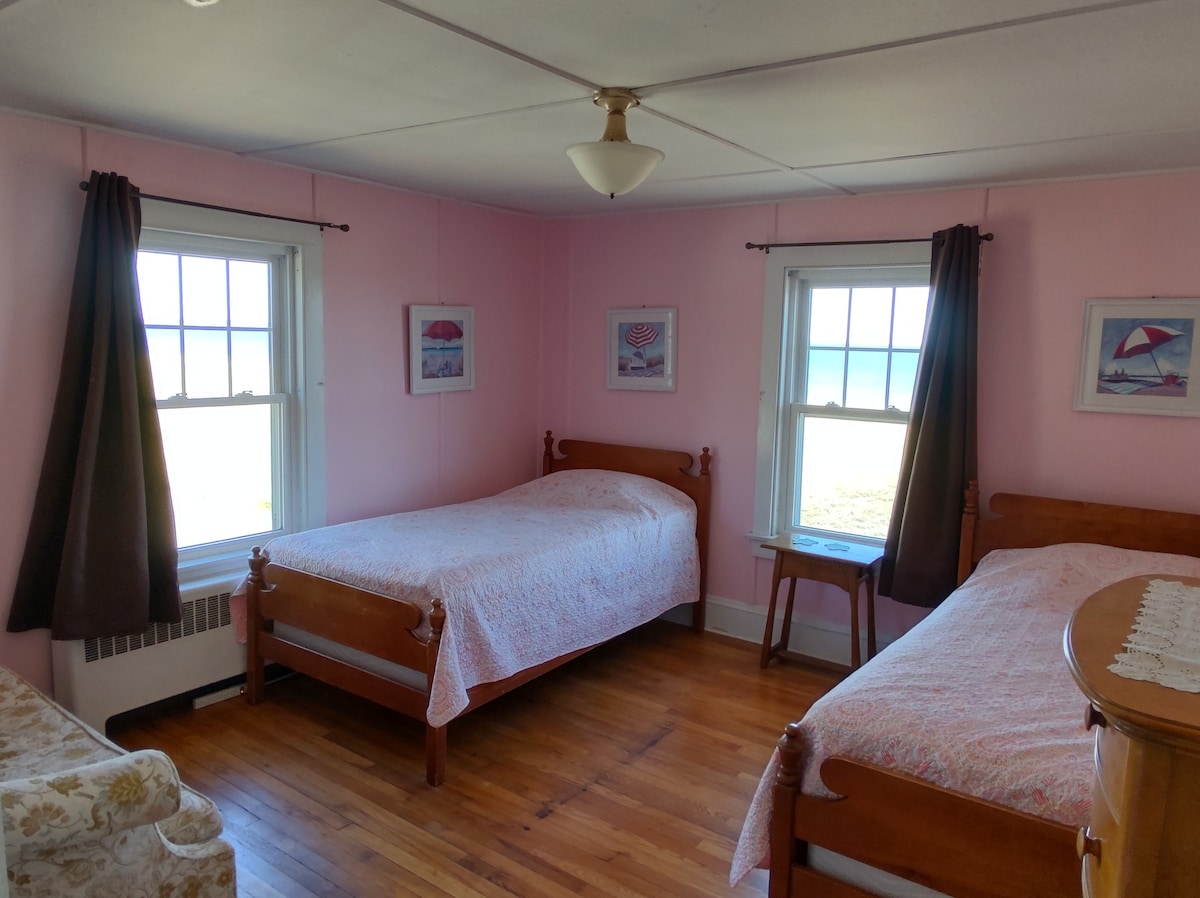 Розовата спална соба има два единечни кревета, поглед кон предниот океан, страничен поглед кон кејот Old Orchard во далечината и затемнети завеси за добар сон. Има кауч за читање (книги за сите возрасти долу!)